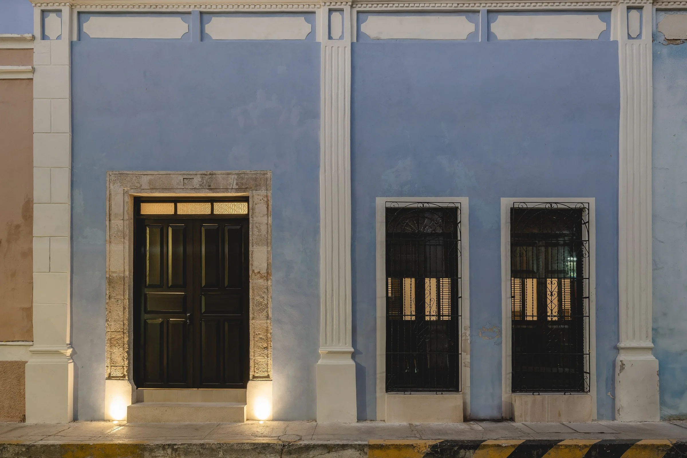 Fachada azul con pilastras blancas de Casa Estrada al anochecer, en la ciudad amurallada de Campeche