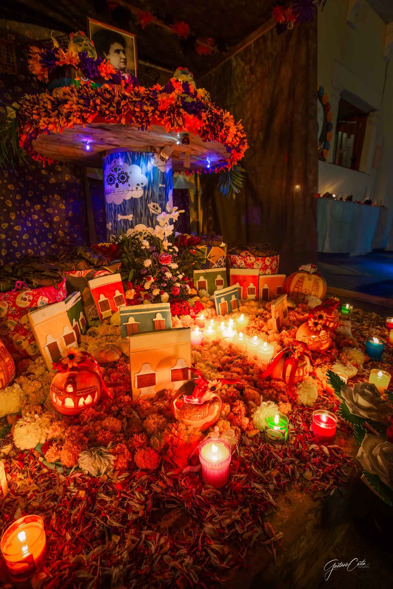 Altar de Hanal Pixán con casitas de colores, velas encendidas y flores de cempasúchil