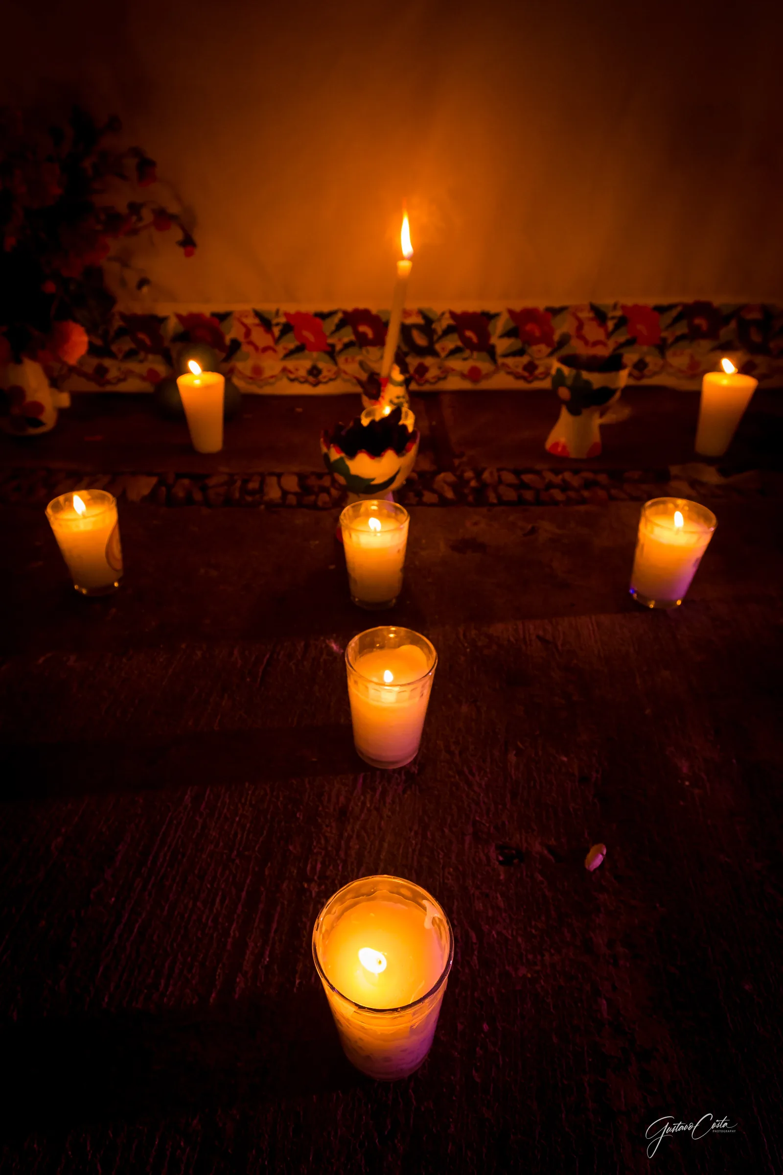 Camino de velas encendidas sobre el piso, frente a un pequeño altar con flores