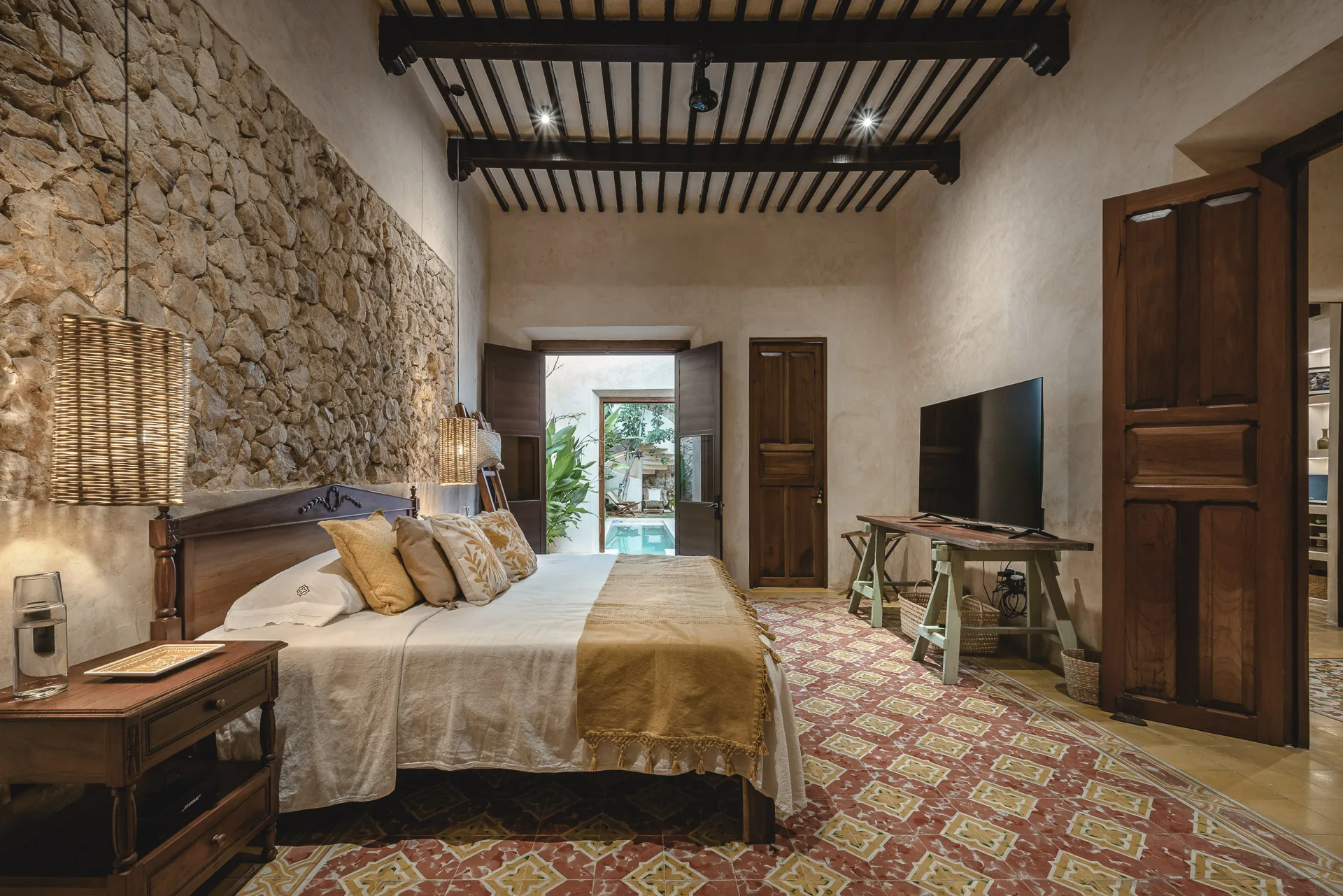 Recámara de La Casa Verde con muro de piedra, techo de vigas y piso de pasta, abierta a la alberca del patio