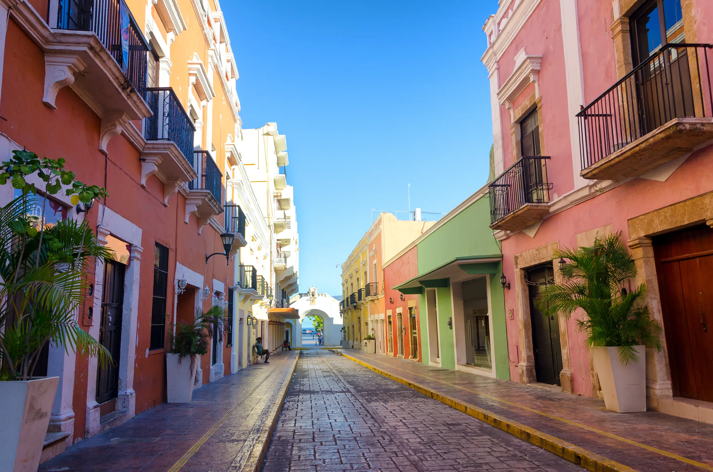 Calle 59 del centro histórico de Campeche, con fachadas naranja, amarilla, verde y rosa y la Puerta de Mar al fondo